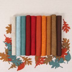 a row of different colored felts with autumn leaves on the bottom one is orange, brown, and blue