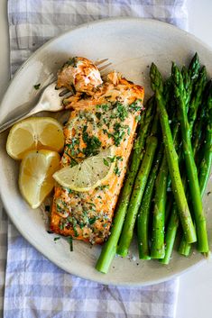 a plate with salmon, asparagus and lemon wedges next to a fork