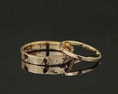 two gold wedding rings sitting next to each other on a black surface with one ring in the middle