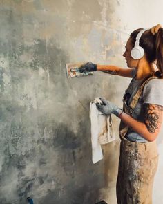 a woman with headphones painting a wall