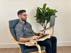 a man sitting in a chair with a laptop on his lap and a potted plant behind him