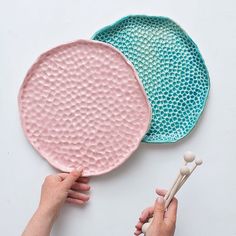 two pink and blue plates are being held by someone's hands with chopsticks