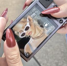 a woman with red nail polish holding up her cell phone to take a picture on the screen