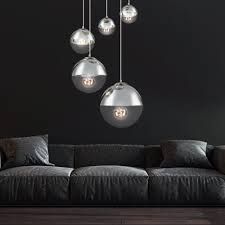 a living room filled with black furniture and hanging light bulbs above the couches in front of a dark wall