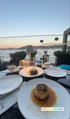 plates with food on them are sitting on a table overlooking the water at sunset or dawn