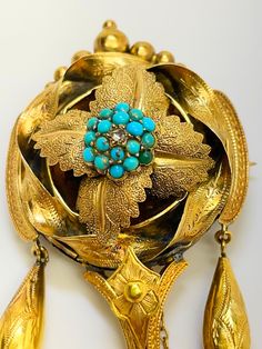 A stunning and eye catching piece of jewellery which is very evocative of its period C1830.  3.5 by 1.5 inches. Does not sound that large  but measure other brooches in your collection to compare. It could convert to a pendant and either way it is quite exceptional. The back holds a large empty locket compartment and most unusually, the gold bound glass is easy to take out and reinsert.  It would have held the hair of a loved one but these days it can hold whatever you want. The central boss is decorated with beads of turquoise with a rose cut diamond to the centre.  The boss is set amongst four veined and textured leaves . These in turn are encircled by a ribbon of gold engraved with leaves. The sides are extended slightly by two curves of gold from which descend two gold torpedos.  The c Traditional Yellow Gold Pendant Brooches, Antique Medallion Brooch Jewelry, Antique Blue Jewelry With Brooch, Victorian Ceremonial Brooch, Victorian Cabochon Ceremonial Jewelry, Traditional Collectible Jewelry Brooch, Turquoise Locket For Wedding Jewelry, Turquoise Locket Jewelry For Wedding, Turquoise Wedding Locket Jewelry