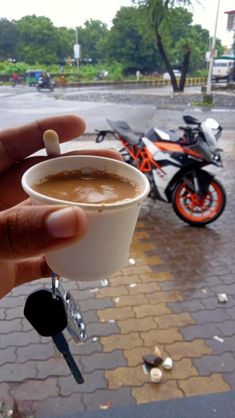 a person holding up a cup of coffee in front of a motorbike on the street