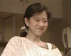 a woman standing in a kitchen next to a stove top oven and smiling at the camera