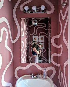 a woman taking a selfie in a bathroom mirror with pink and white wallpaper