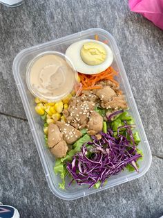 a plastic container filled with meat and veggies next to an egg on top