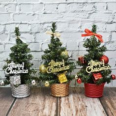 three small christmas trees sitting next to each other on top of a wooden table in front of a brick wall