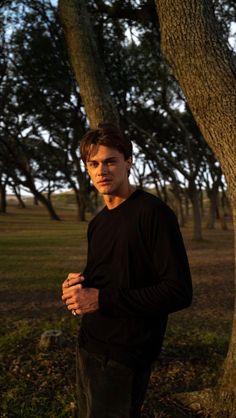 a young man standing next to a tree