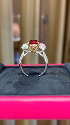 a red and white diamond ring sitting on top of a pink velvet display case in front of a window