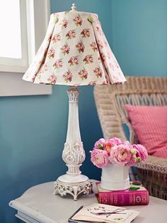 a table with a lamp, books and flowers on it next to a wicker chair