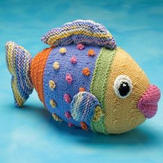 a knitted toy fish sitting on top of a blue surface with multicolored stripes