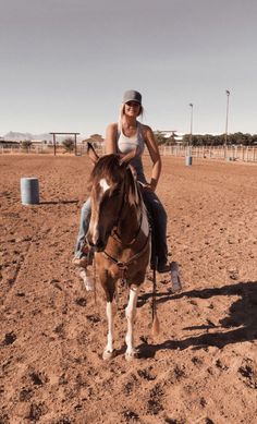 a woman riding on the back of a brown and white horse in a dirt field