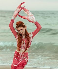 a woman with red hair is sitting on the beach and holding her hands above her head