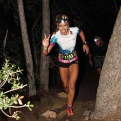 a woman running through the woods at night with her hands up in the air and smiling