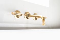 two brass faucets on the side of a white wall