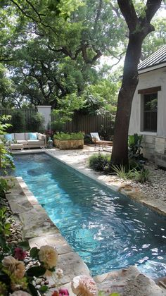 a small pool in the middle of a garden with flowers and trees around it, next to a house