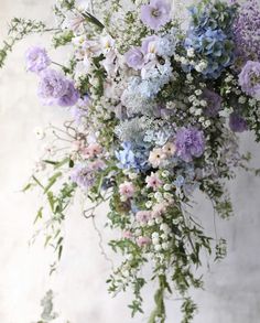 a bunch of flowers hanging from the side of a wall with greenery on it