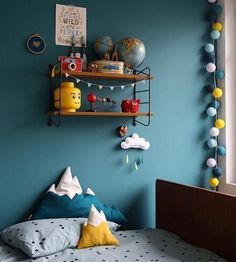 a bed room with a neatly made bed next to a blue wall and shelves filled with toys