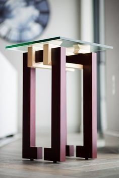 a glass table with two wooden legs and a clock in the background