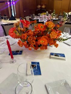 a vase filled with orange flowers on top of a white table cloth covered dining room table