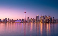 the city skyline is lit up at night with its lights reflecting in the water and bright blue sky