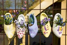 five pairs of shoes hanging on a fence with flowers in the bottom one is painted white