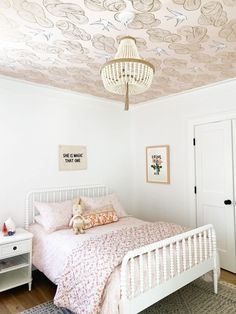 a white bed sitting under a chandelier in a bedroom