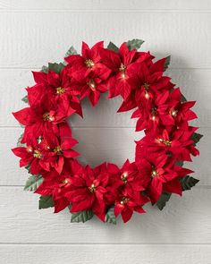 a wreath with red poinsettias and green leaves on a white brick wall