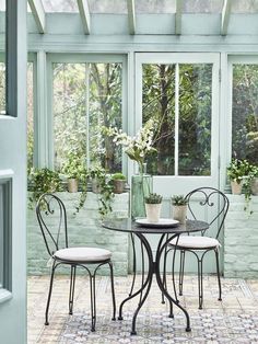 two chairs and a table in front of a window with potted plants on it