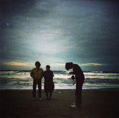 three people are standing on the beach near the water