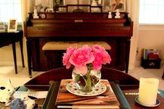 a vase with pink flowers on a table in front of a piano and other items