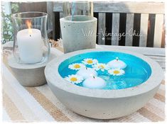 a bowl filled with water sitting on top of a table next to a lit candle