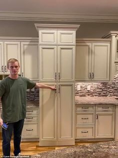 a man is standing in the middle of a kitchen with white cabinets and granite counter tops