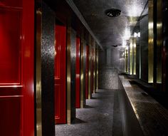 an empty hallway with red doors and tiled walls in the center is lit by spotlights