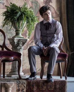 a young man sitting on top of a chair next to a vase filled with flowers