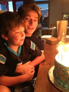 a man and boy sitting in front of a cake with lit candles