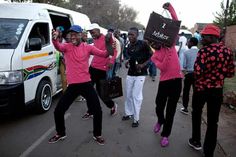 several people in pink shirts and white pants are dancing on the street with their luggage