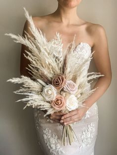 a woman in a wedding dress holding a bouquet of white and pink flowers with feathers