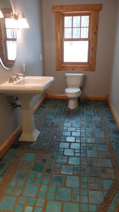 a bathroom with blue and green tiles on the floor, sink, toilet and window