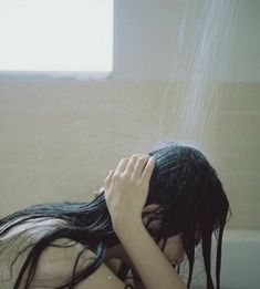 a woman is sitting in the bathtub with her head down and hair flowing out