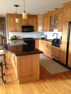 a kitchen with wooden cabinets and black counter tops, an island in between the stove and refrigerator