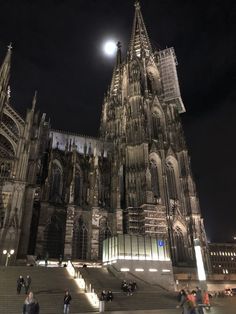 people are walking up and down the steps in front of an old cathedral at night