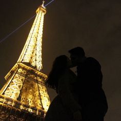 a man and woman kissing in front of the eiffel tower at night time