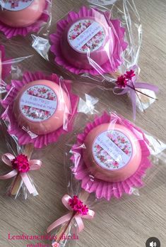 four pink cupcakes wrapped in cellophane and sitting on a wooden table