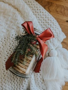 a glass jar filled with cookies on top of a white blanket next to a red bow