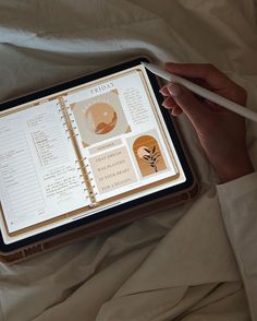 a person is holding an open notebook and pen in their hand while laying on a bed